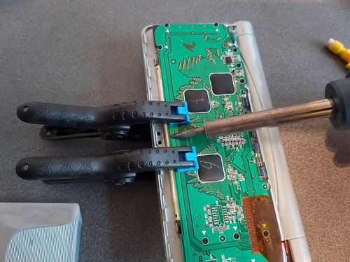 Photo of a soldering iron being used to heat up the back of the organiser's PCB. Two spring clamps are clipped to either side of where it is being applied